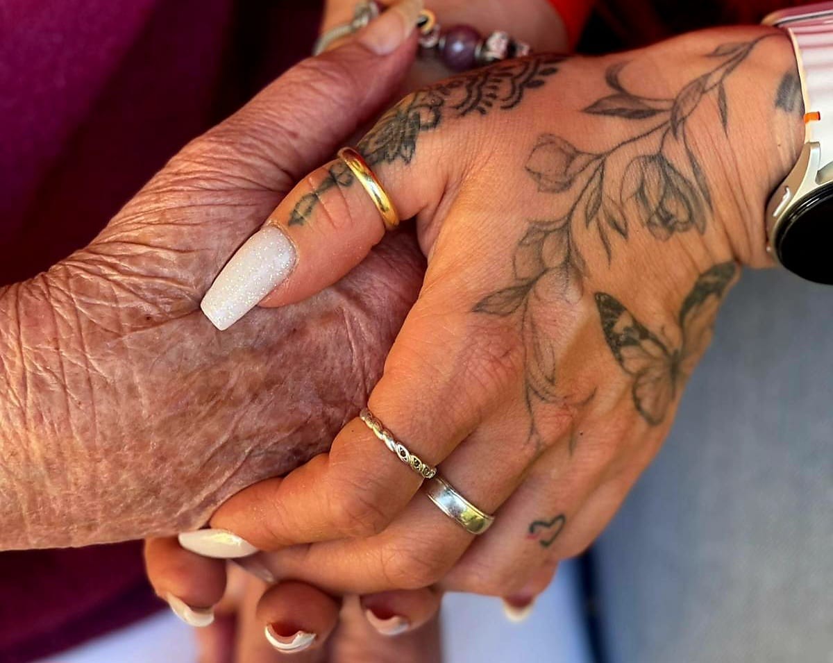 Pflegekraft hält liebevoll die Hand einer Seniorin